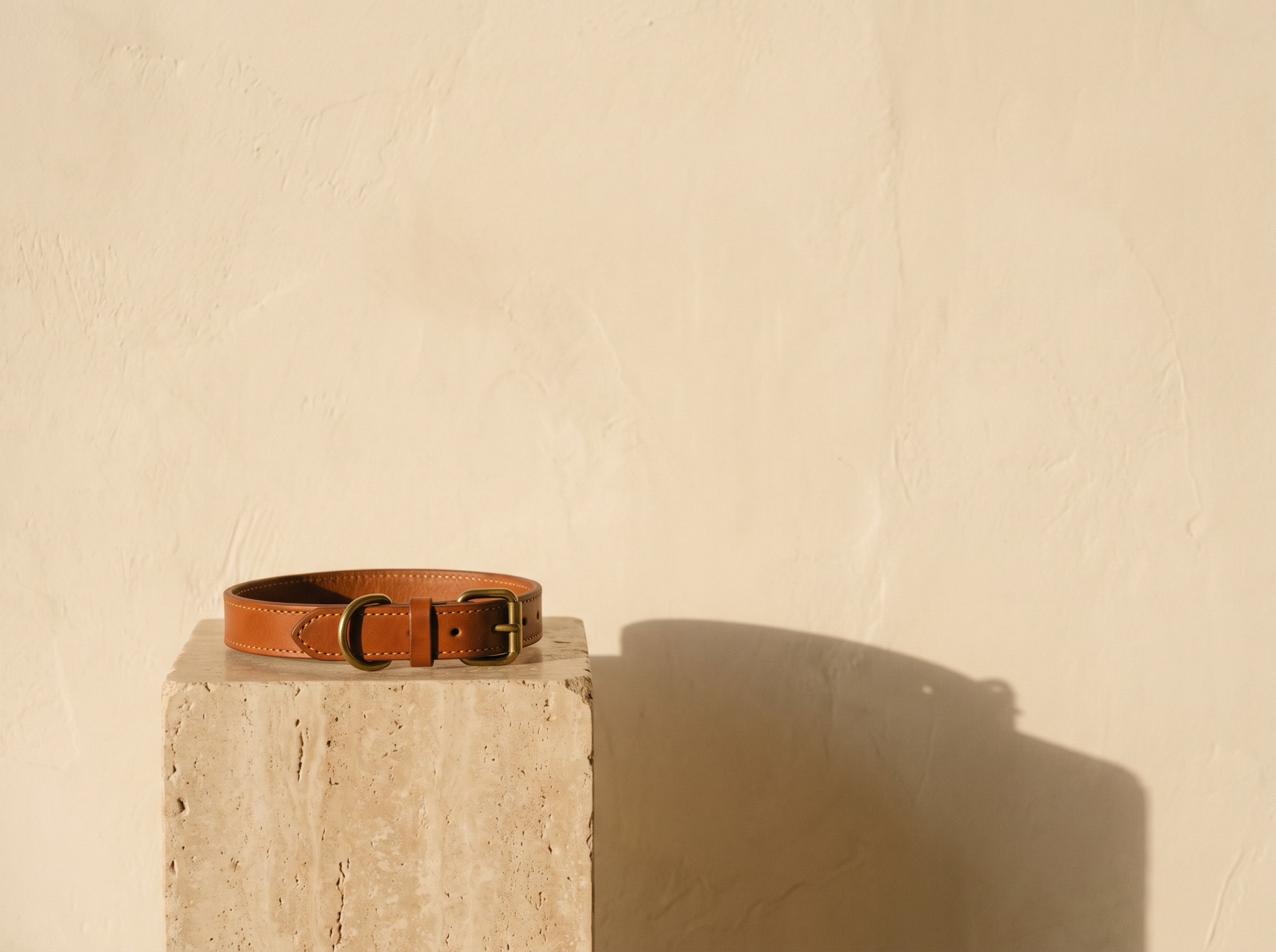 Un collar de cuero coñac sobre un pedestal de travertino